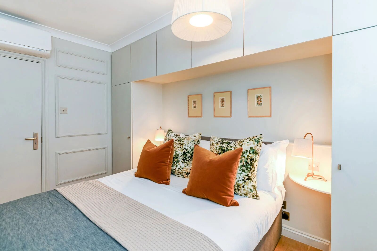 A bedroom with a bed, pillows, a bedside table, a lamp, and framed pictures on the wall.