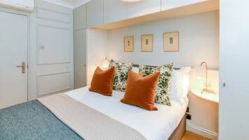 A bedroom with a bed, pillows, a bedside table, a lamp, and framed pictures on the wall.