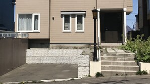Una casa de dos pisos con techo oscuro, revestimiento color beige y una entrada frontal con escalones.