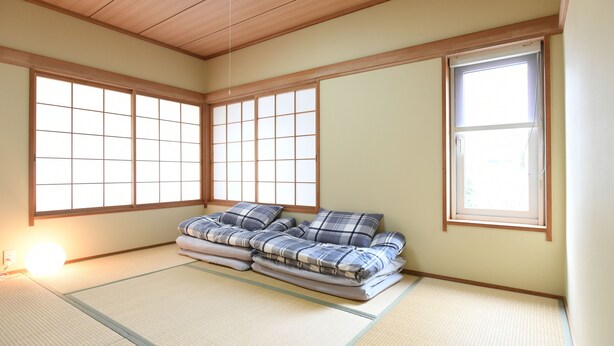 Una habitación con tatami, un futón, ventanas amplias y un techo tradicional japonés.