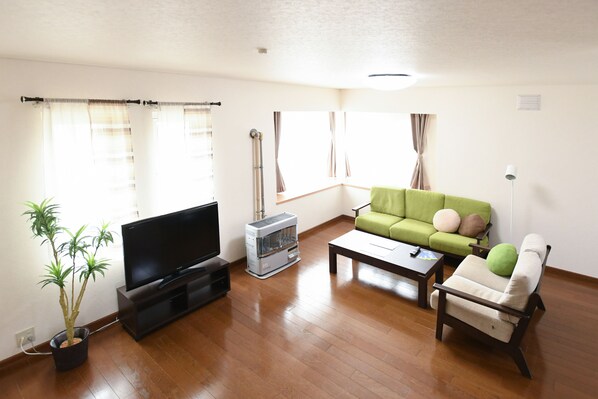 A living room with a flat-screen TV, a green sofa, a white armchair, a coffee table, and a potted plant. - Cozy Villa Otaru (Otaru)