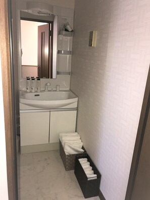 A narrow bathroom with a sink, mirror, and toiletries. There is a towel rack and a small trash bin. - Cozy Villa Otaru (Otaru)