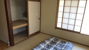 Una habitación con suelo de tatami, una cama futón, un armario corredero y una ventana con celosía de shoji.