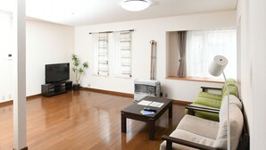 Una sala de estar con televisor de pantalla plana, un calefactor, una mesa de centro, un sofá y una ventana con cortinas.