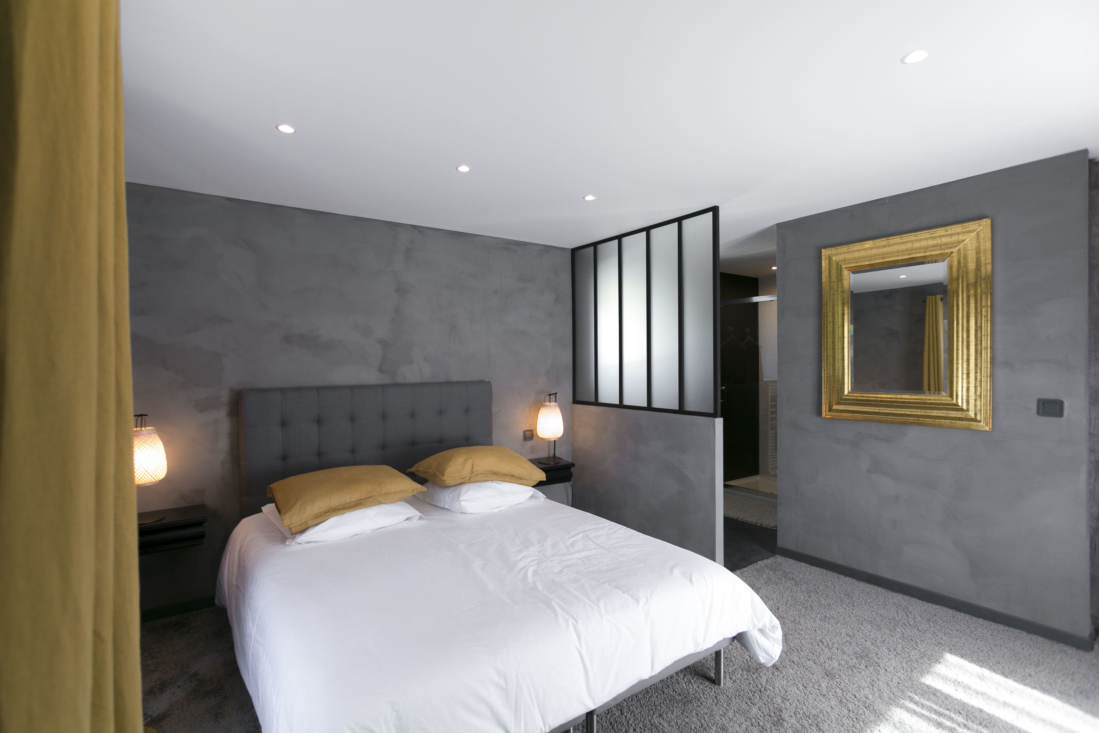 A modern bedroom with a large bed, two bedside lamps, a nightstand, and a mirror with a gold frame.