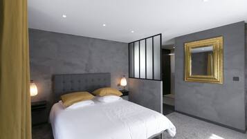 A modern bedroom with a large bed, two bedside lamps, a nightstand, and a mirror with a gold frame.