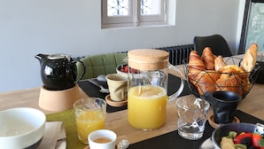 Una mesa de desayuno con diversas opciones de comida y bebidas, incluyendo cruasanes, zumo de naranja y un bol de fruta.