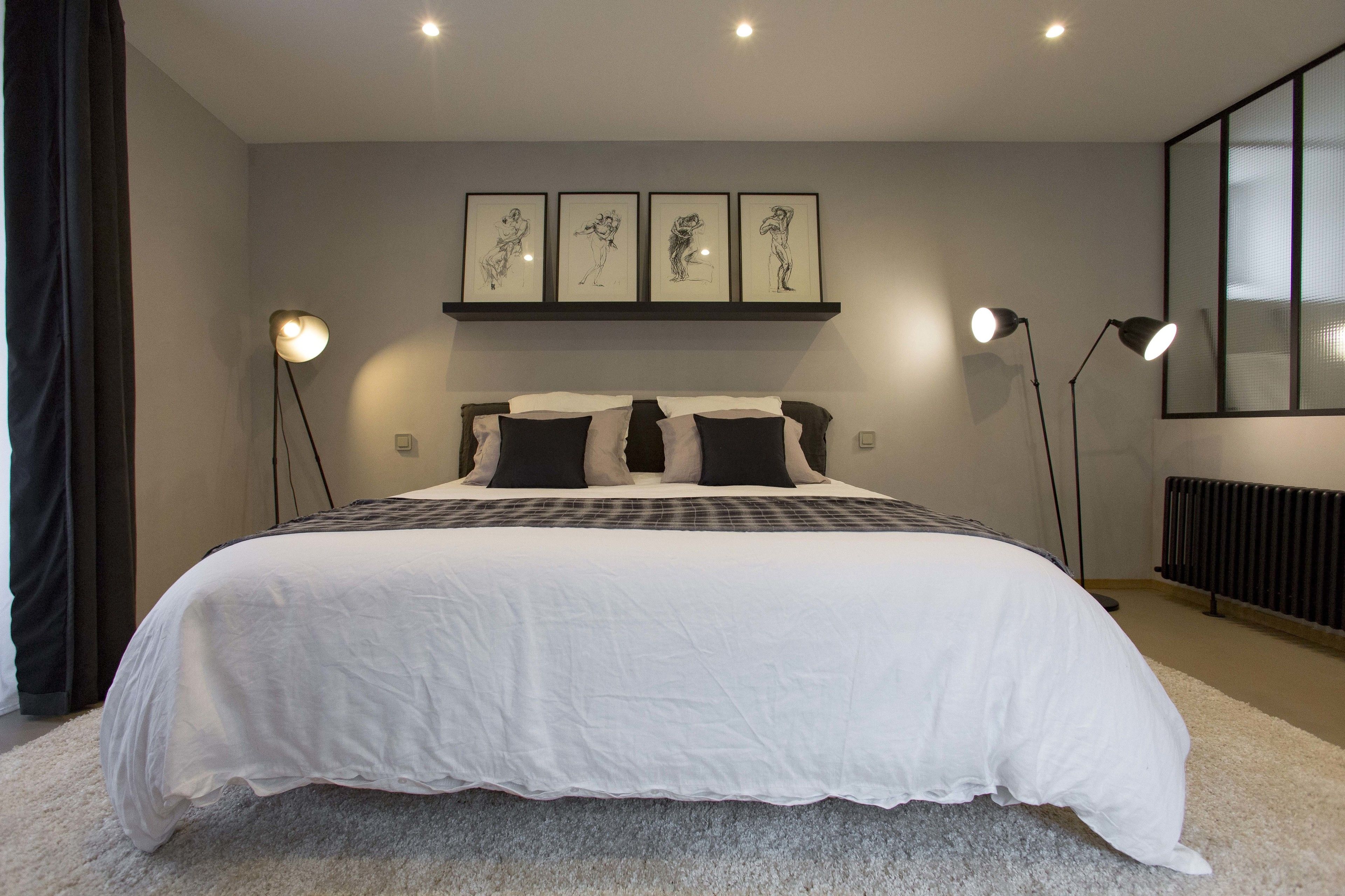 Un dormitorio con una cama grande, un cabecero decorado con una obra de arte, dos lámparas de noche y un radiador.