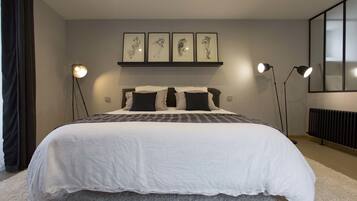 Un dormitorio con una cama grande, un cabecero decorado con una obra de arte, dos lámparas de noche y un radiador.