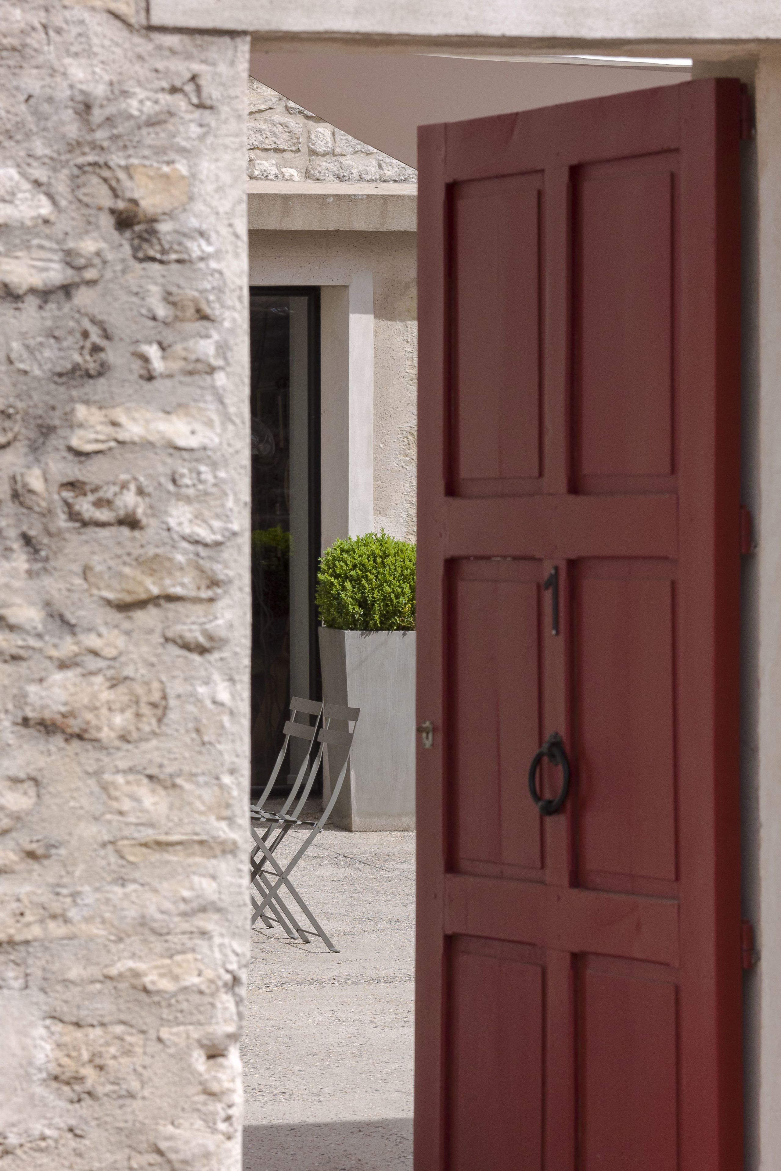 A red door with a black handle, a stone wall, and a small potted plant visible through the door.