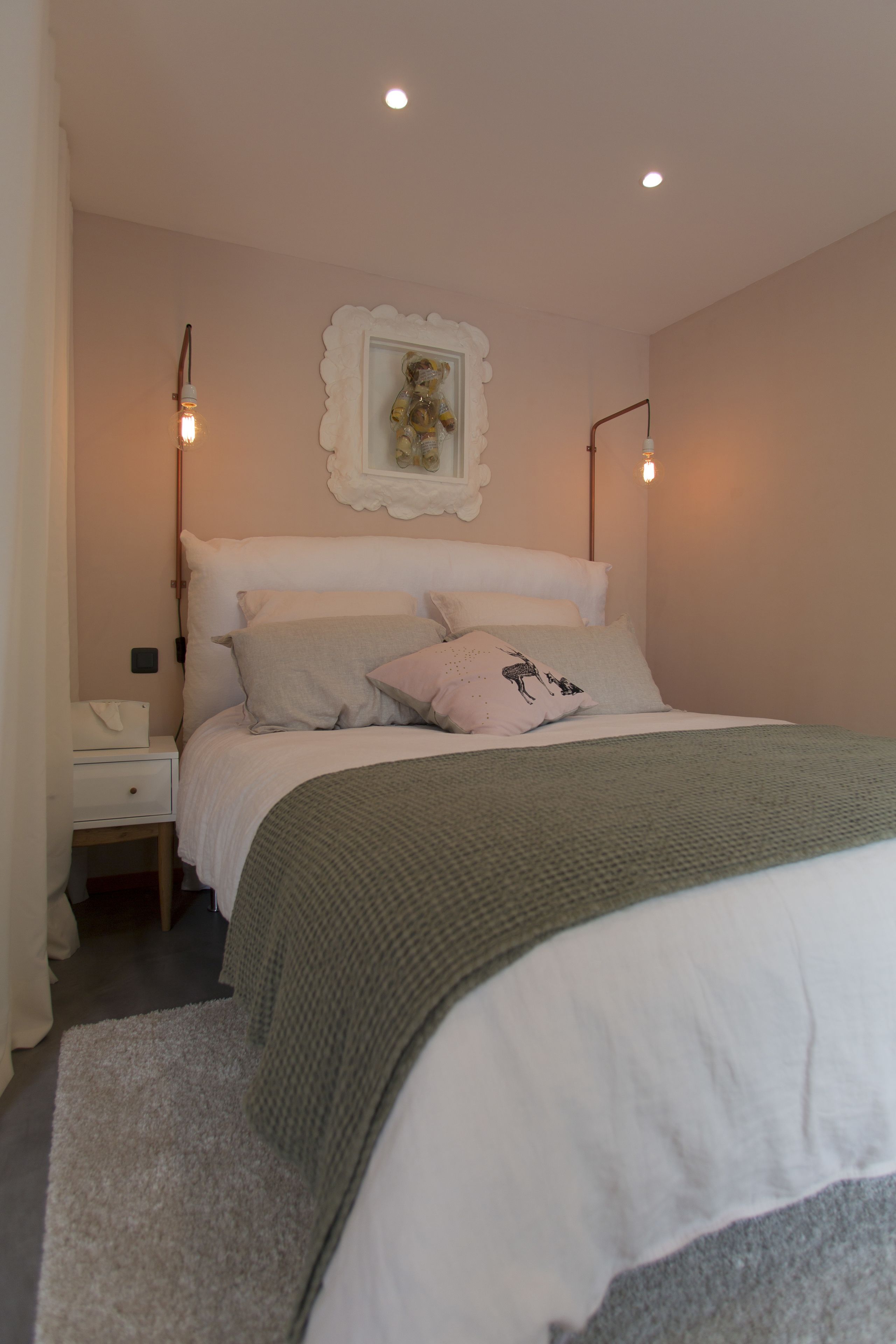 Une chambre à coucher bien rangée, avec un lit, des oreillers, une table de chevet et un luminaire fixé au mur.