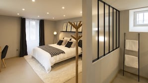 Un dormitorio moderno con una cama grande, una mesita de noche, una lámpara de pie y vistas al exterior a través de una ventana.