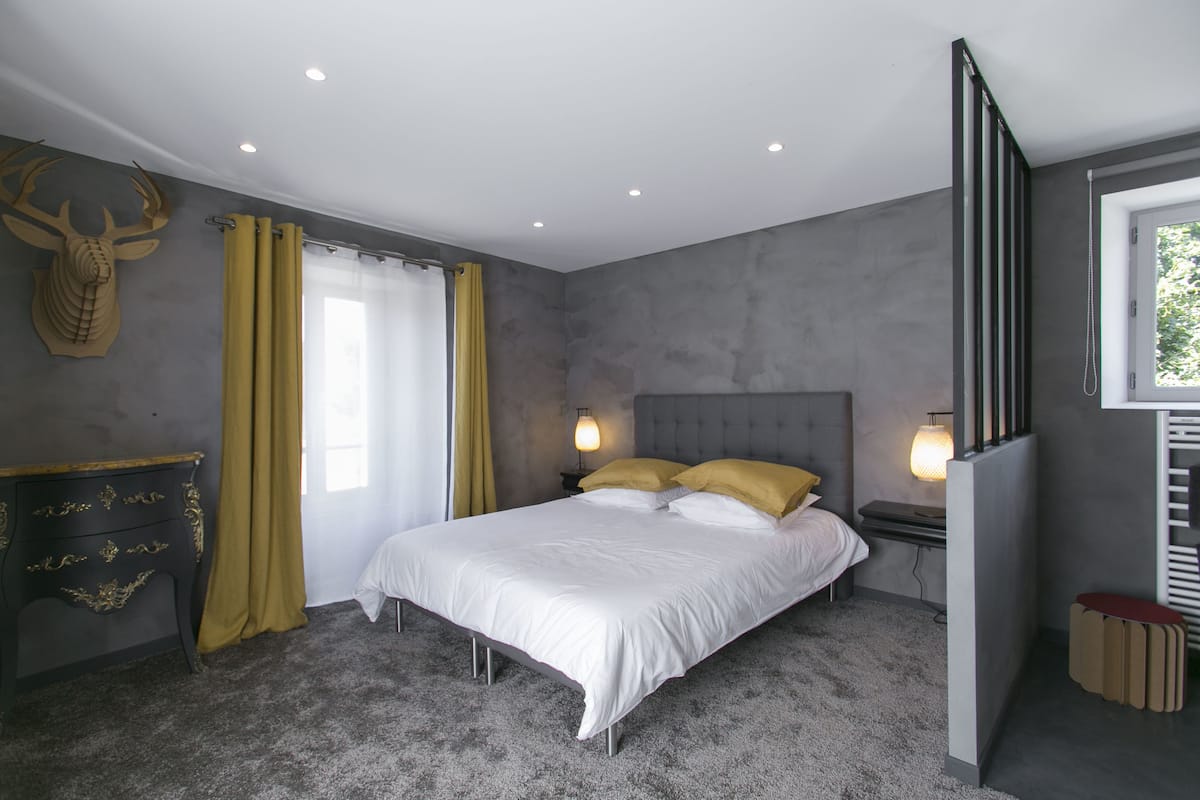 Ein Schlafzimmer mit einem Bett, Vorhängen, einem an der Wand befestigten Hirschgeweih und einem Fenster.