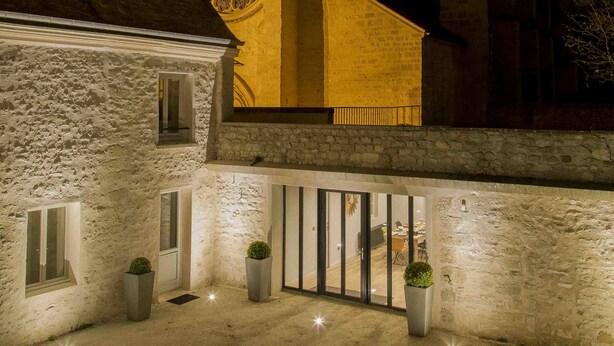 Un edificio histórico con una torre de reloj, muros de piedra y un patio con plantas en macetas.