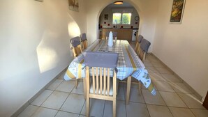 Un espace repas avec une longue table, des chaises et une cuisine en arrière-plan.