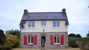 Une maison à deux étages avec une façade en pierre, des volets rouges et un toit recouvert de tuiles.