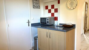 Une petite cuisine équipée d’un four à micro-ondes, d’une petite poubelle et d’un meuble en bois.