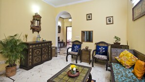 A room with a ceiling fan, a sofa, a chair, a small table with a vase of flowers, and a potted plant. - Prakash Kutir B&B (New Delhi)