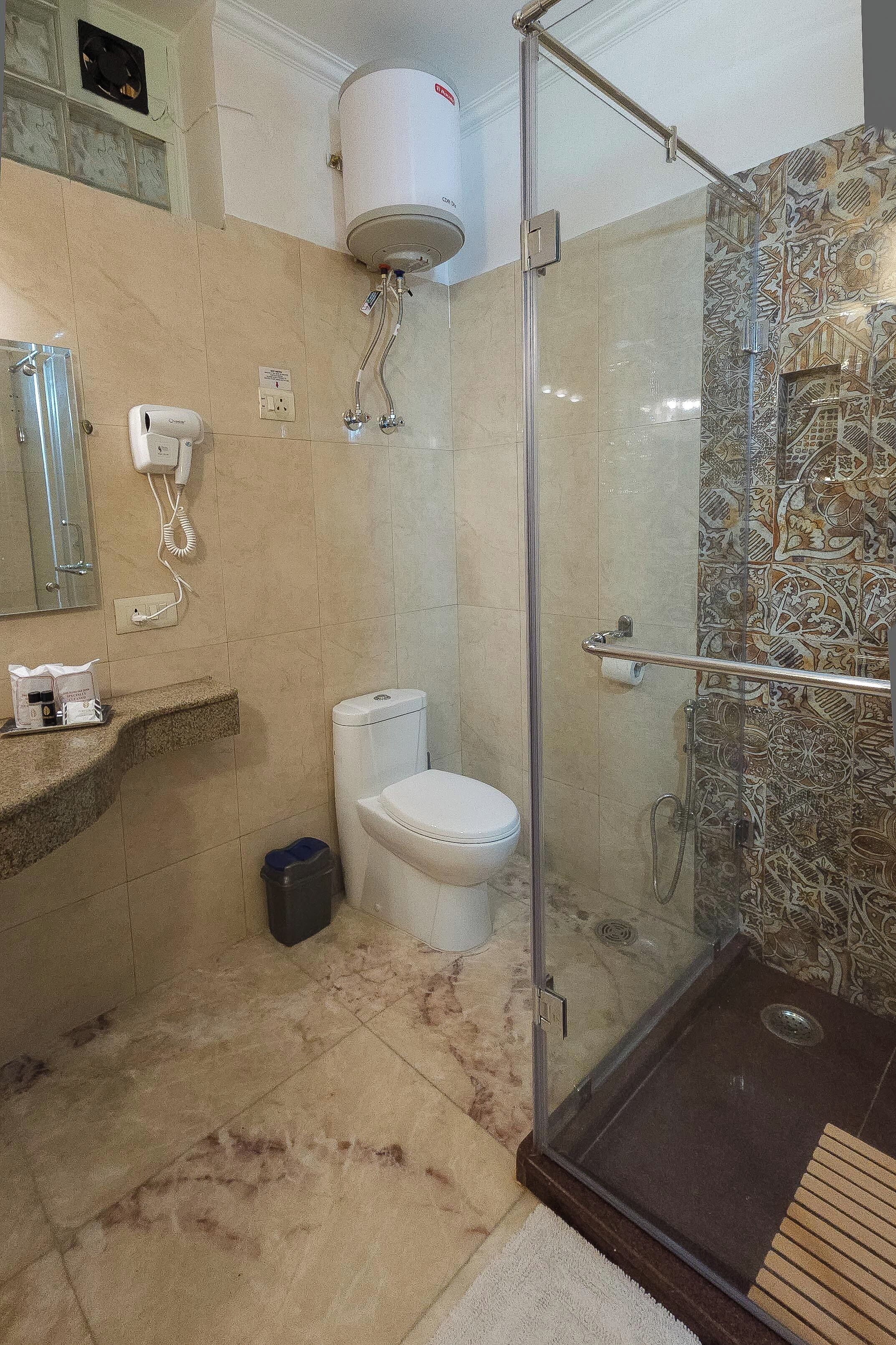 Un baño con inodoro, ducha con puerta de vidrio, suelo de mármol y un perchero para toallas.