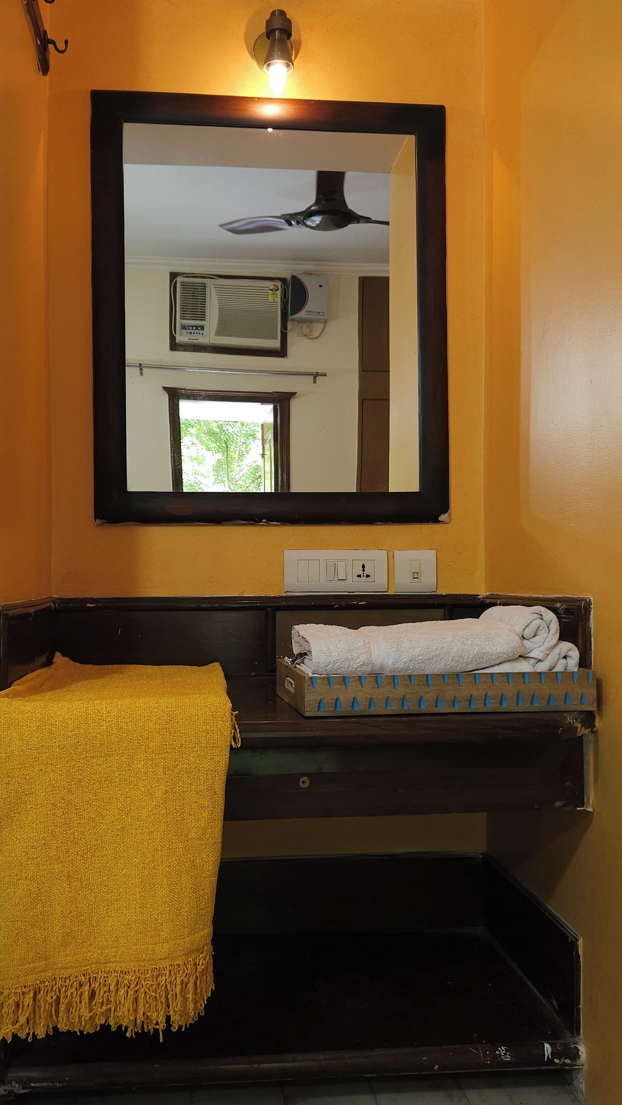Un baño con tocador de madera, espejo, ventilador de techo y ventana con vistas a follaje.