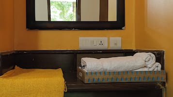Un baño con tocador de madera, espejo, ventilador de techo y ventana con vistas a follaje.