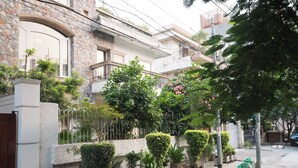 A residential building with a stone facade, multiple balconies, and a well-maintained garden with various plants and a small tree with pink flowers. - Prakash Kutir B&B (New Delhi)