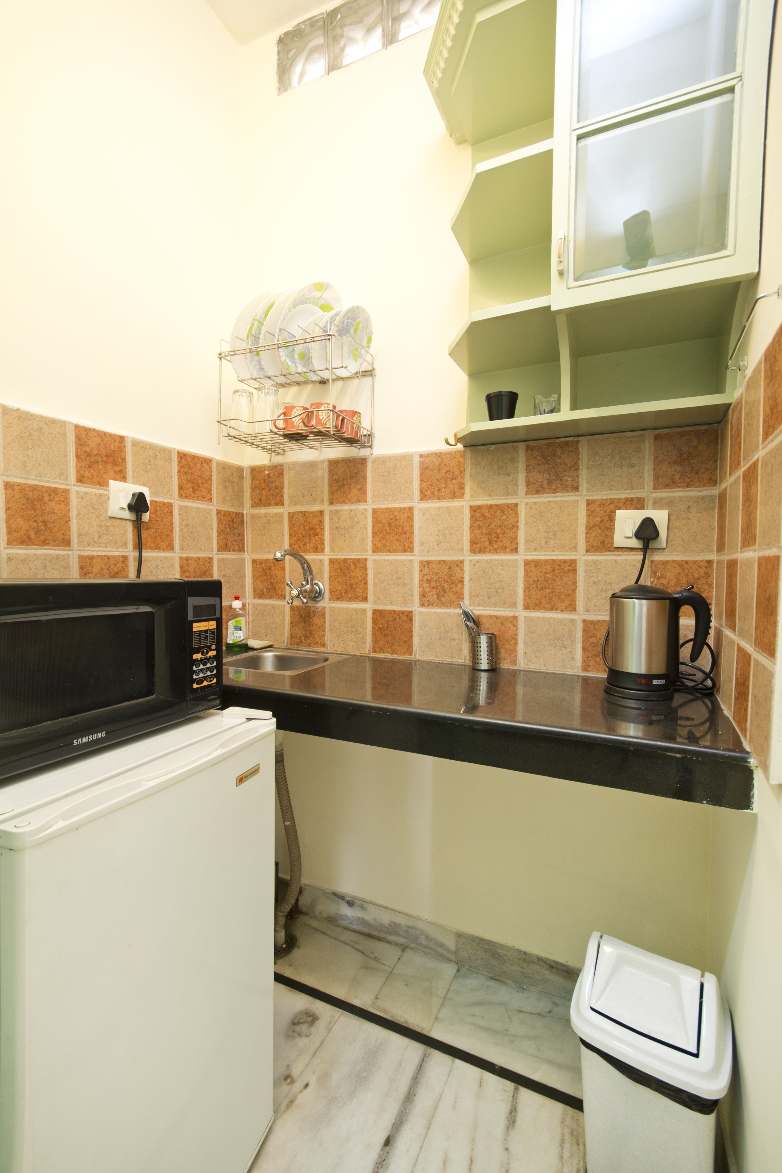 A compact kitchen with a microwave, sink, and a small trash bin.