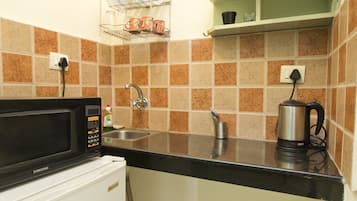 A compact kitchen with a microwave, sink, and a small trash bin.