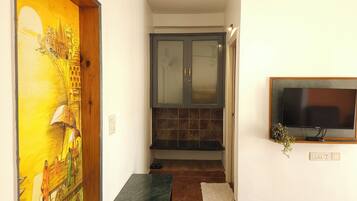 Um corredor com uma porta de madeira adornada por um mural colorido, um armário escuro com portas de vidro e uma televisão fixada na parede.