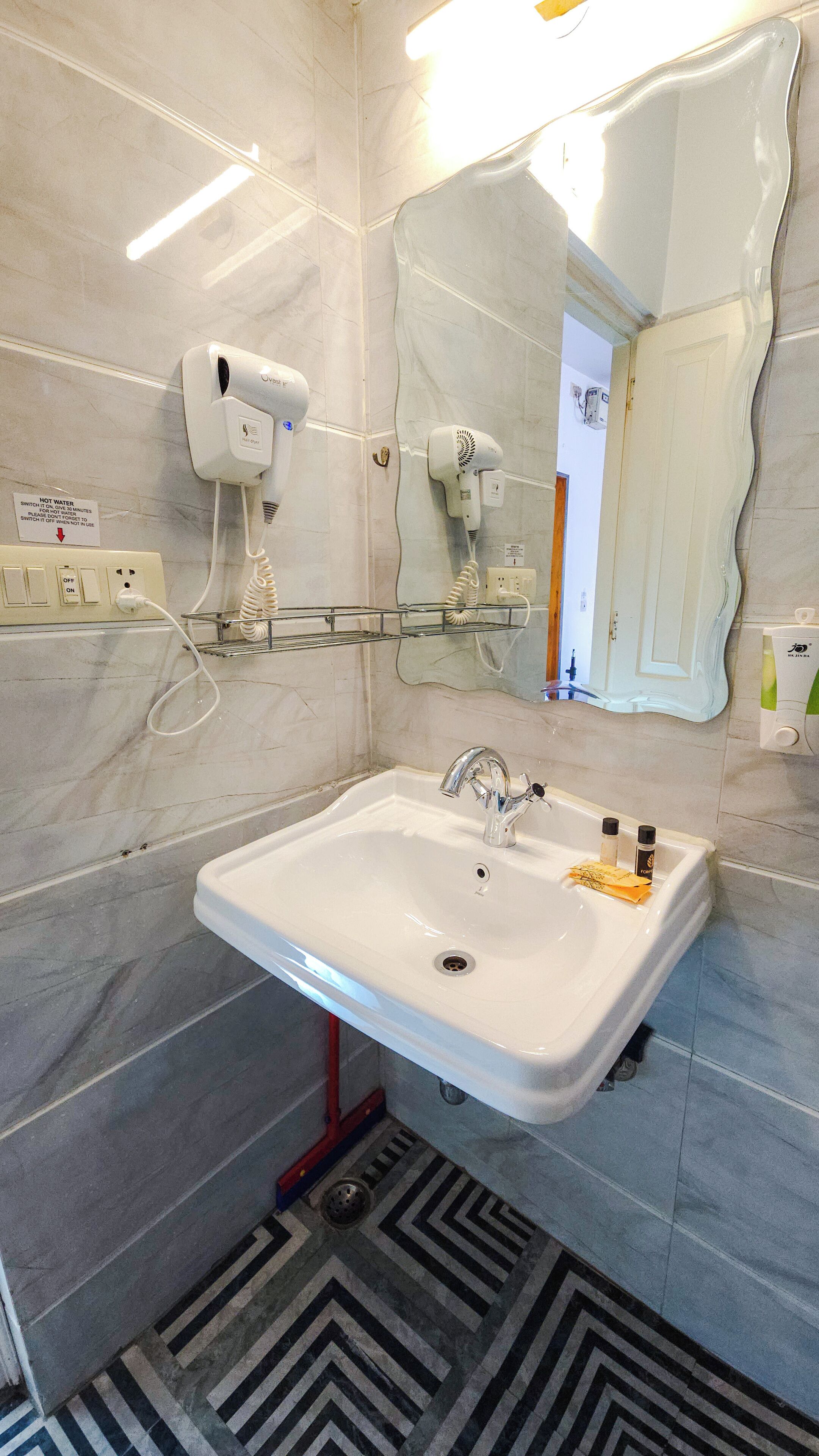 A bathroom with a white sink, a mirror, and two hair dryers mounted on the wall.