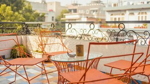 A terrace with orange metal chairs and a glass table, overlooking a cityscape with buildings and greenery. - Prakash Kutir B&B (New Delhi)
