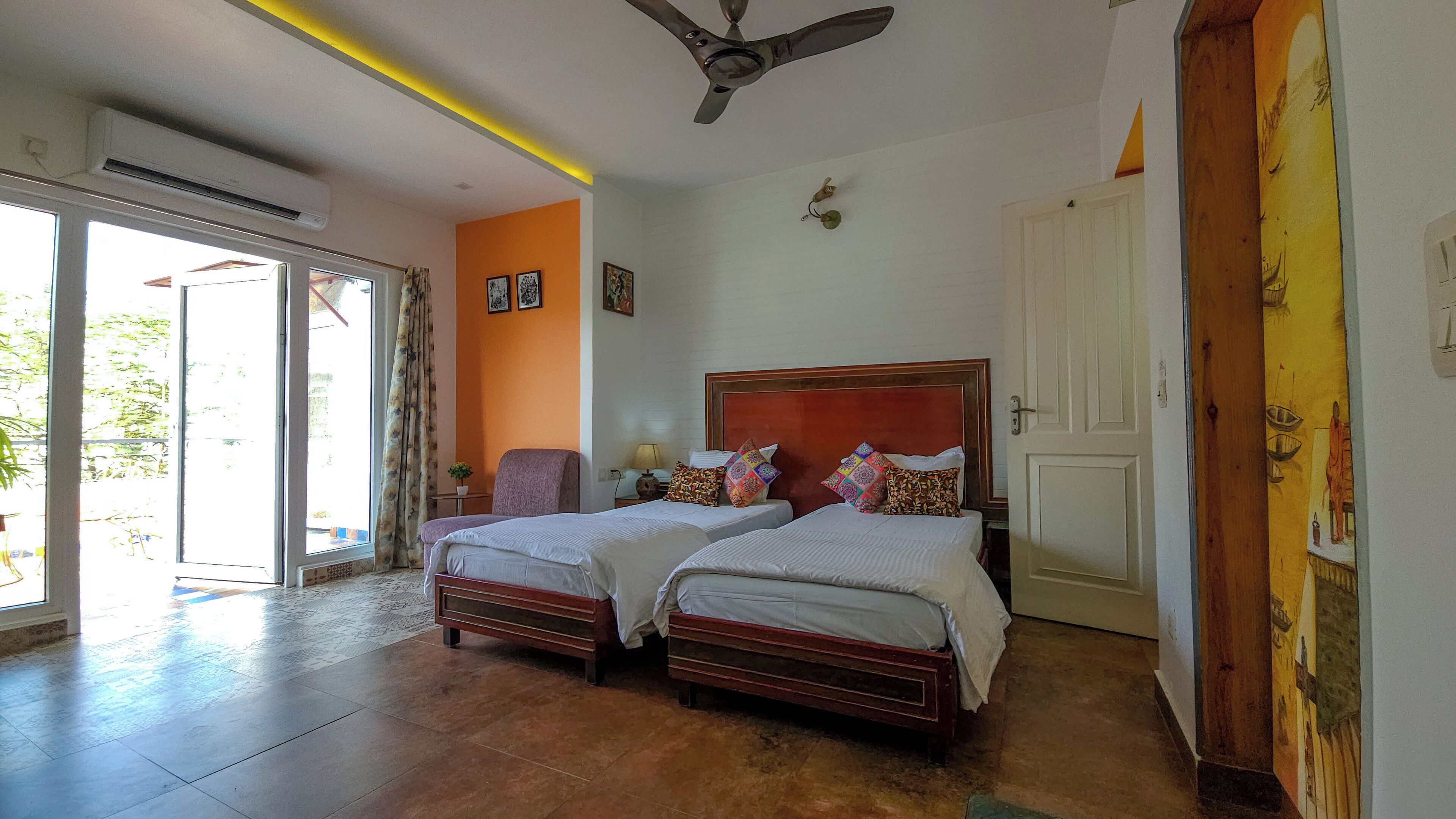 A hotel room with two beds, a ceiling fan, a sliding glass door to the outside, and a door with a decorative panel.