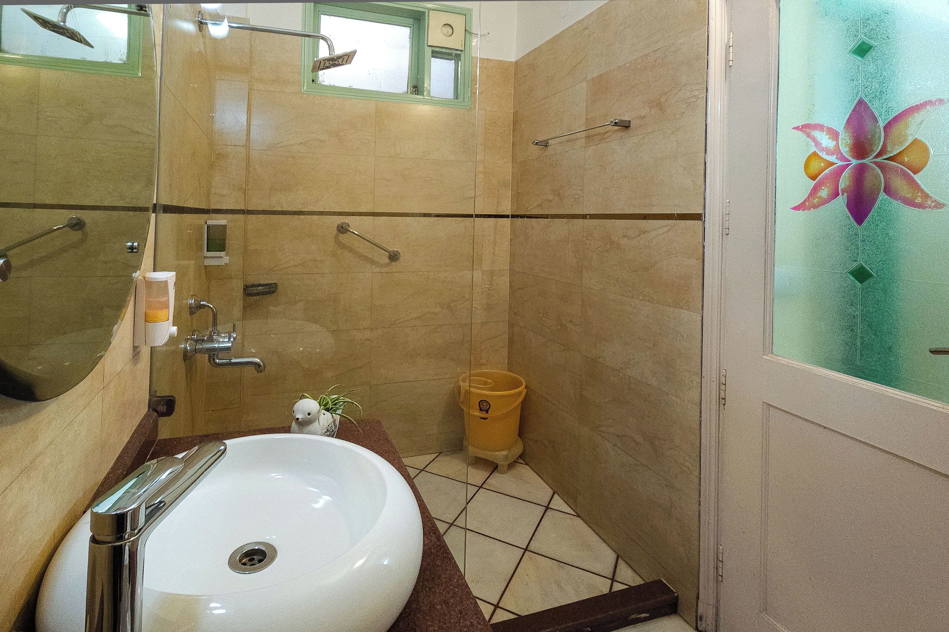 A bathroom with a white sink, a glass shower enclosure, and a yellow trash bin.