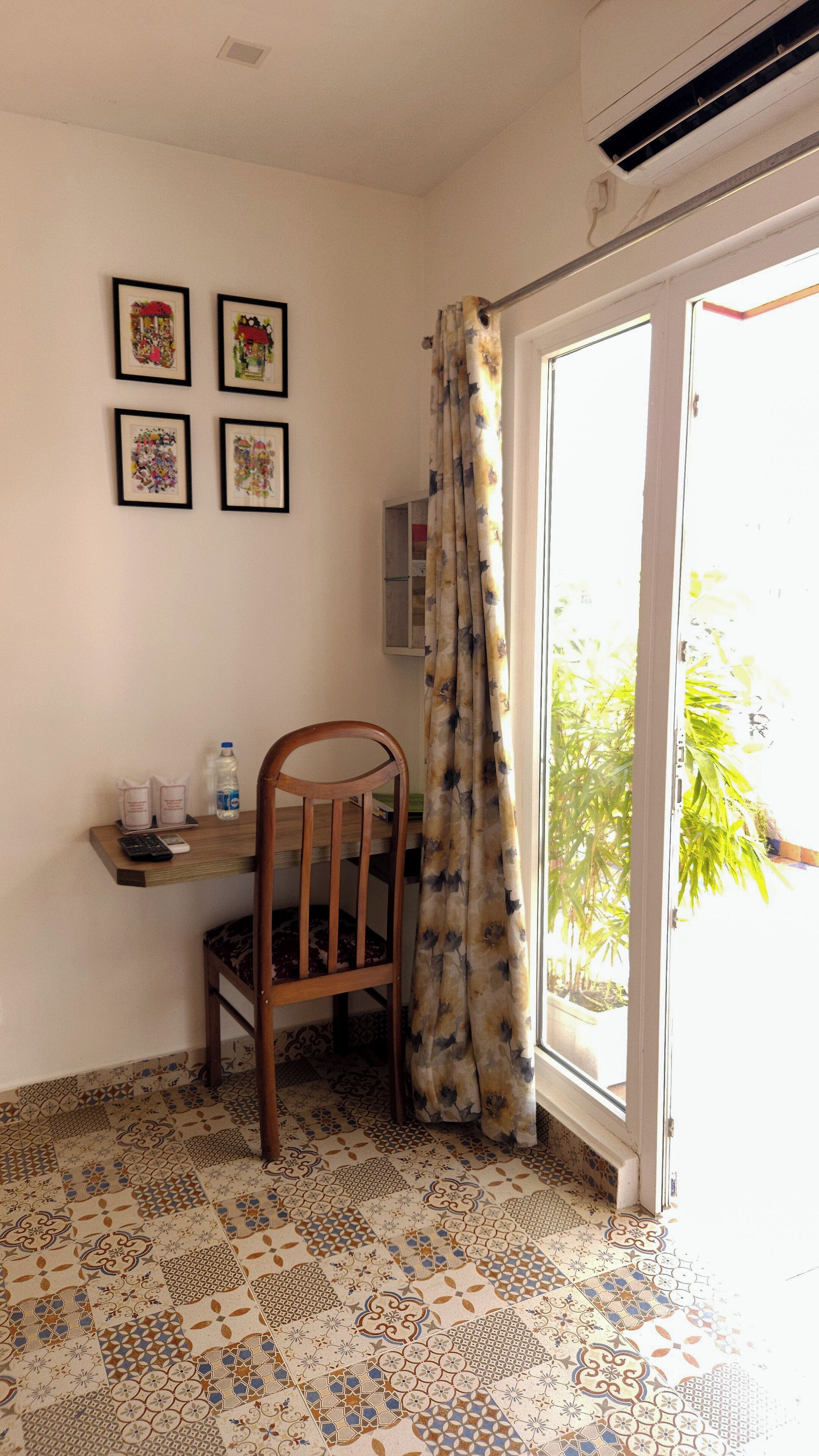 A room with a wooden chair, a small table with a water bottle, framed pictures on the wall, and a patterned floor.
