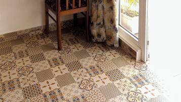 A room with a wooden chair, a small table with a water bottle, framed pictures on the wall, and a patterned floor.