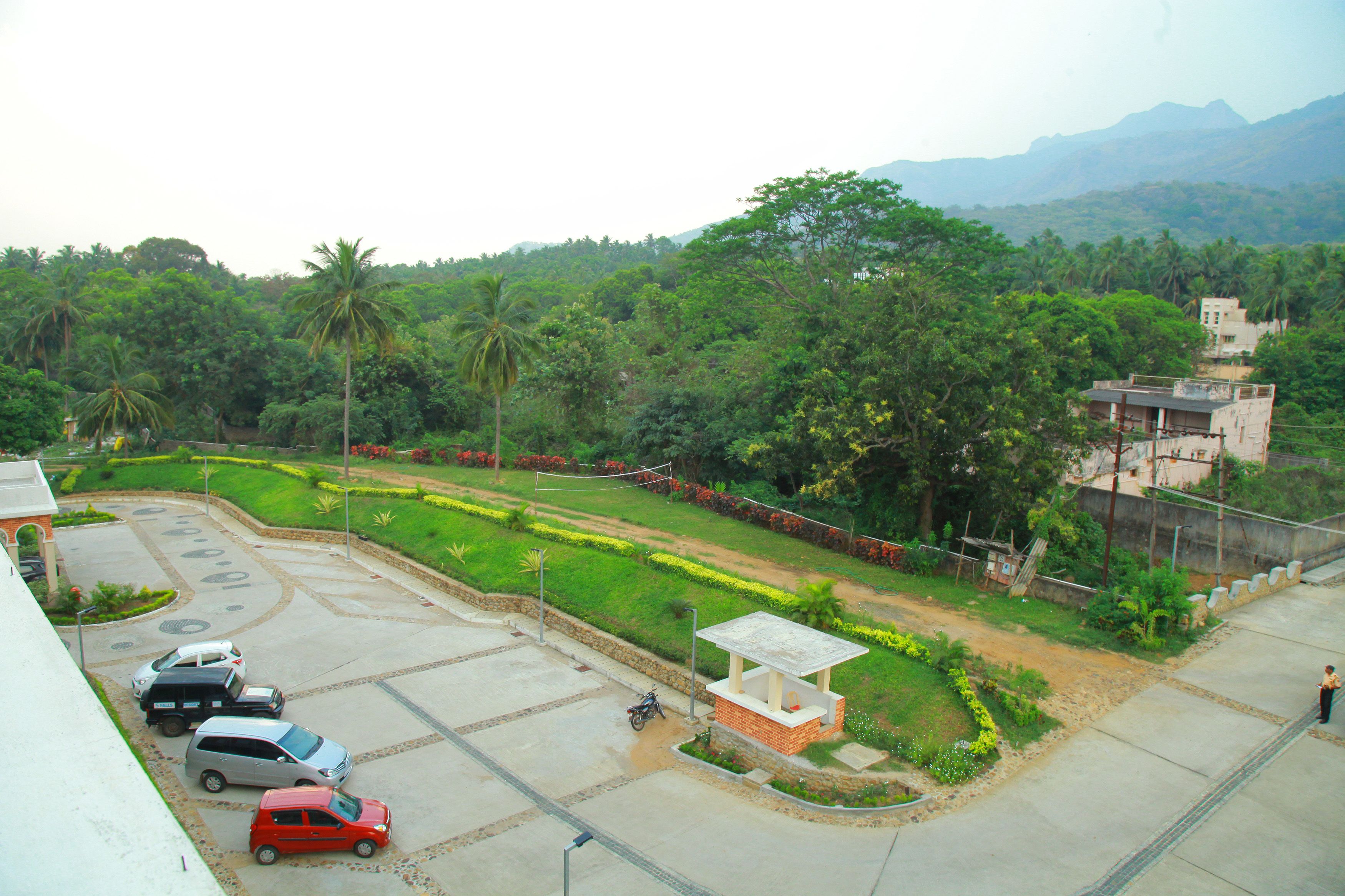 A parking area with several cars, a small building, and lush greenery in the background.
