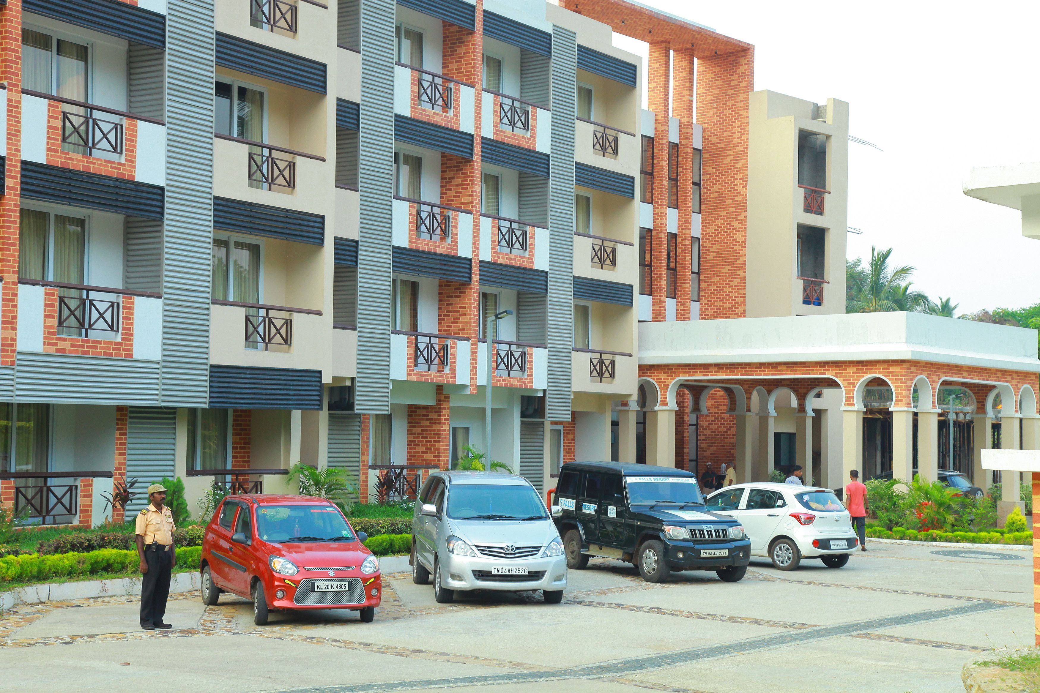 Un edificio residencial de varios pisos con balcones, zona de estacionamiento y guardia de seguridad.