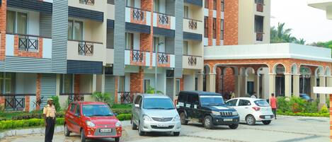 Un edificio residencial de varios pisos con balcones, zona de estacionamiento y guardia de seguridad.