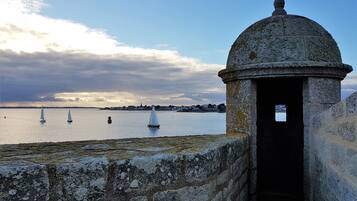 A stone structure with a dome and an open doorway, overlooking a calm body of water with sailboats.