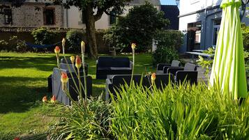 Un espace jardin avec des sièges extérieurs, un arbre et un bâtiment en arrière-plan.