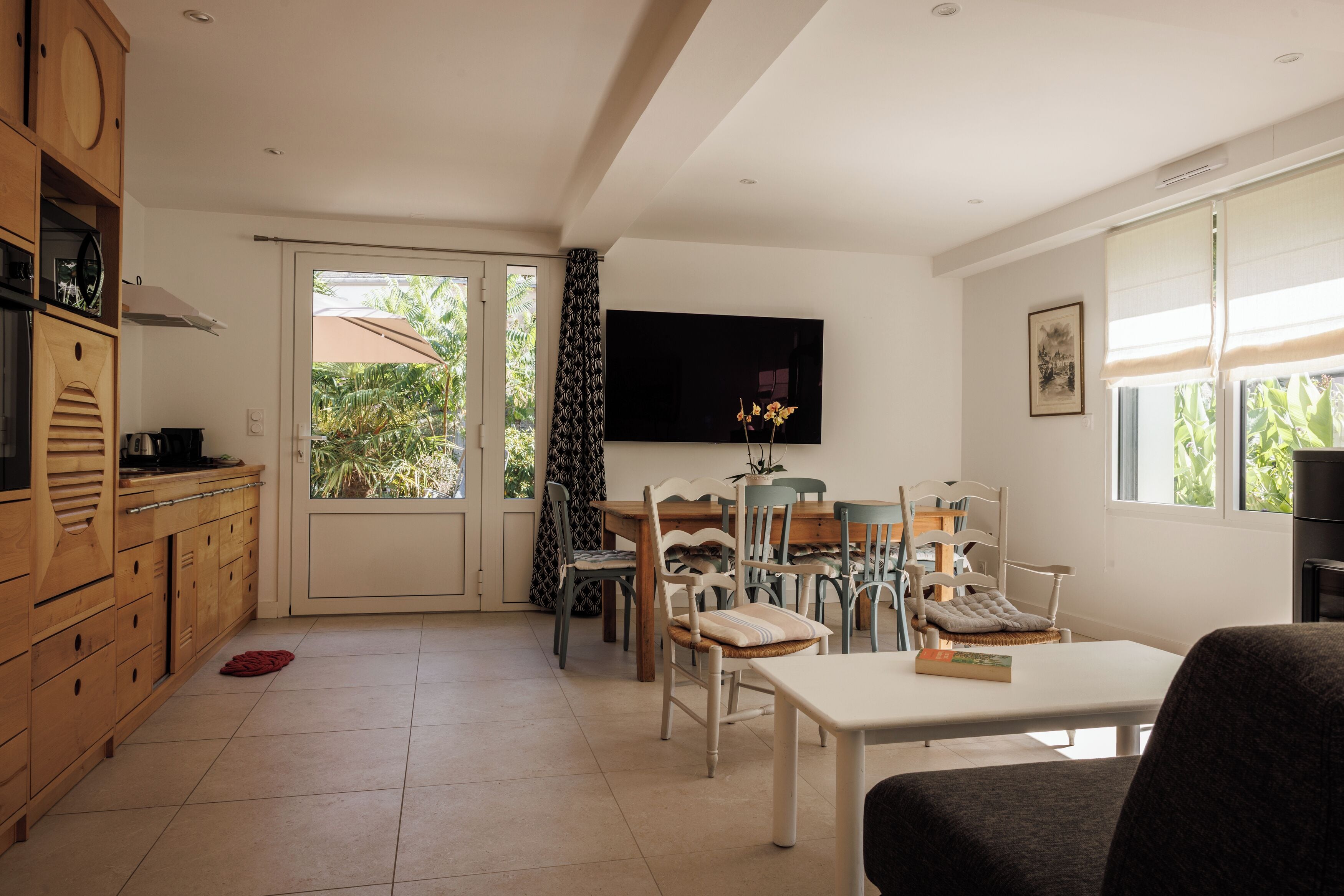 A spacious living area with a dining table, chairs, a television, and a kitchen area with wooden cabinets and a countertop.