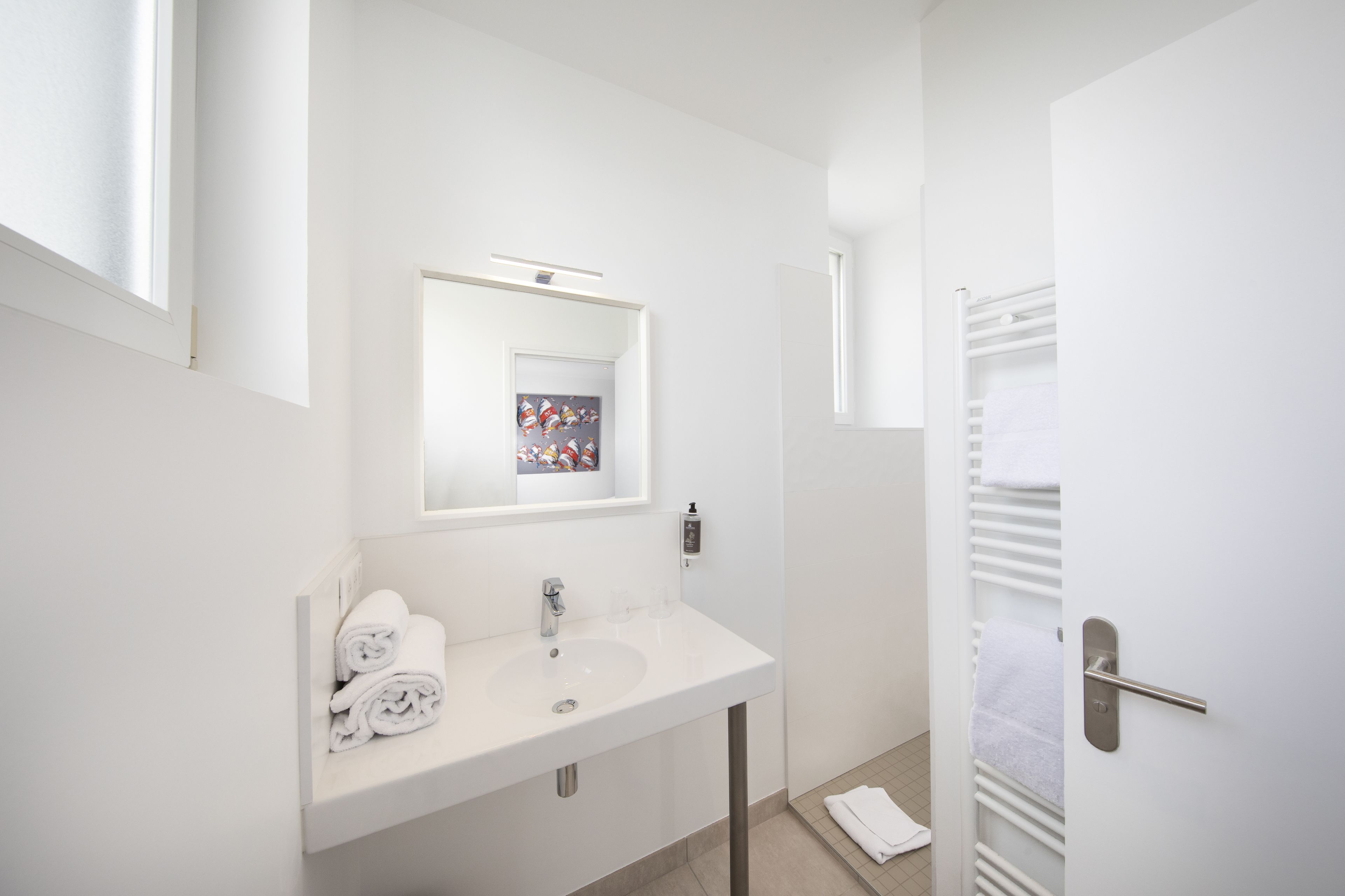 A modern bathroom with a white sink, mirror, and towel rack.