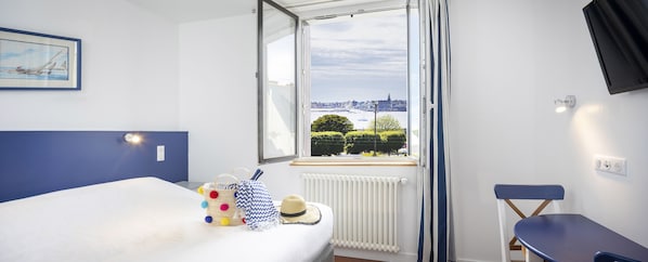Habitación de hotel con cama, vista panorámica de la ciudad a través de una ventana, radiador y una silla.