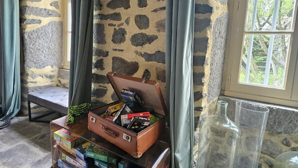 A cozy room with a stone wall, a window with a view of trees, a suitcase with board games, and a bench. - Datcha Anastasia (Besse-et-Saint-Anastaise)