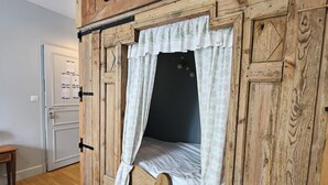 A rustic wooden room with a bed featuring a white canopy and floral curtains. - Datcha Anastasia (Besse-et-Saint-Anastaise)