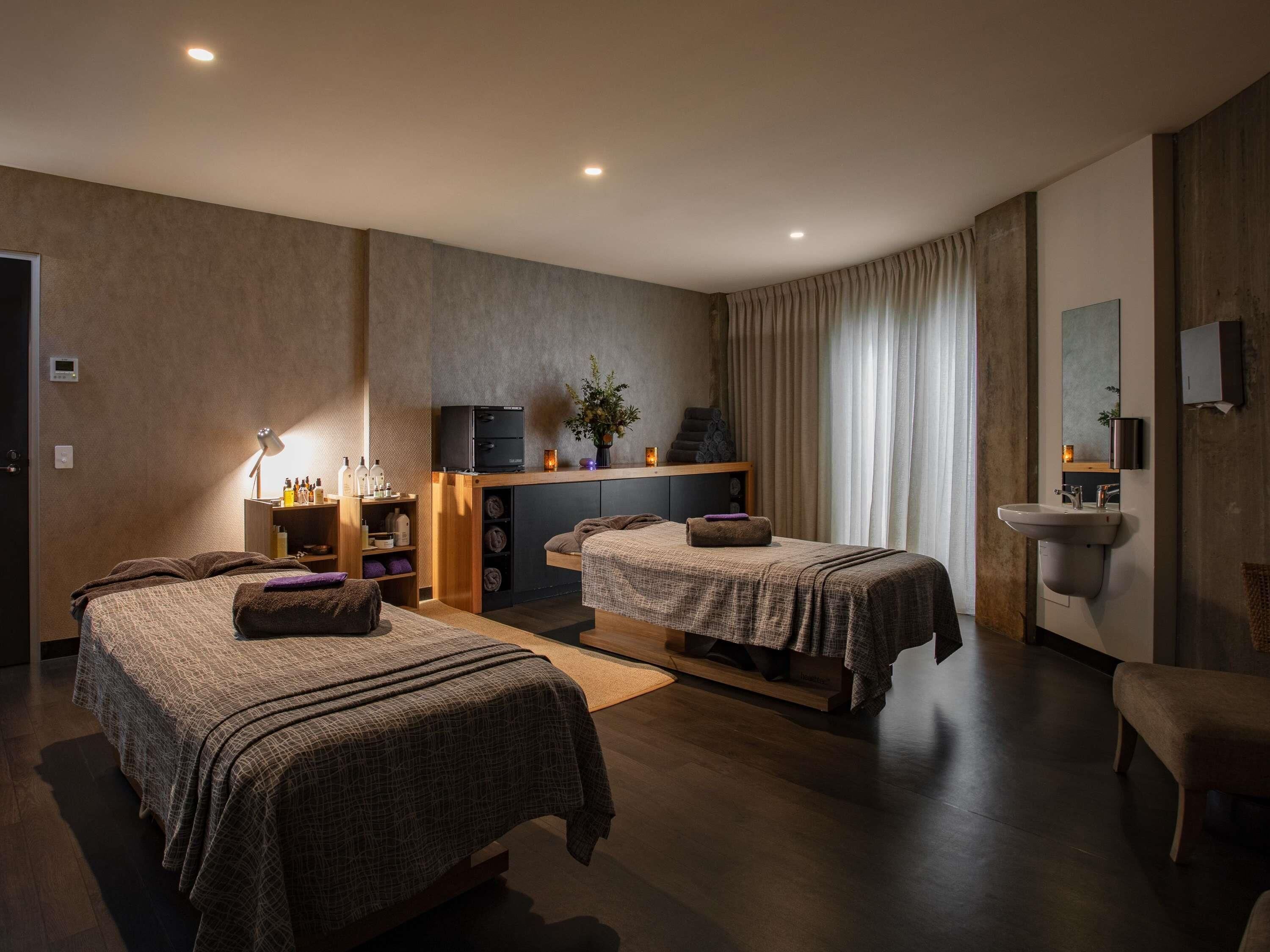 A hotel room with two beds, a desk, a TV, a mirror, and a bathroom.