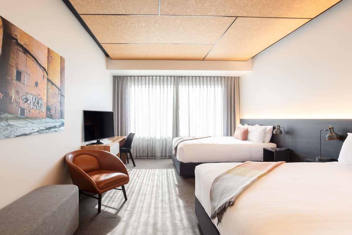 A hotel room with two beds, a desk, a chair, a TV, and a painting on the wall.