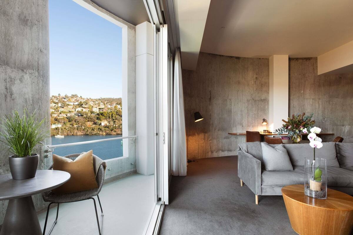 A modern living room with a balcony overlooking a body of water and a hilly landscape.