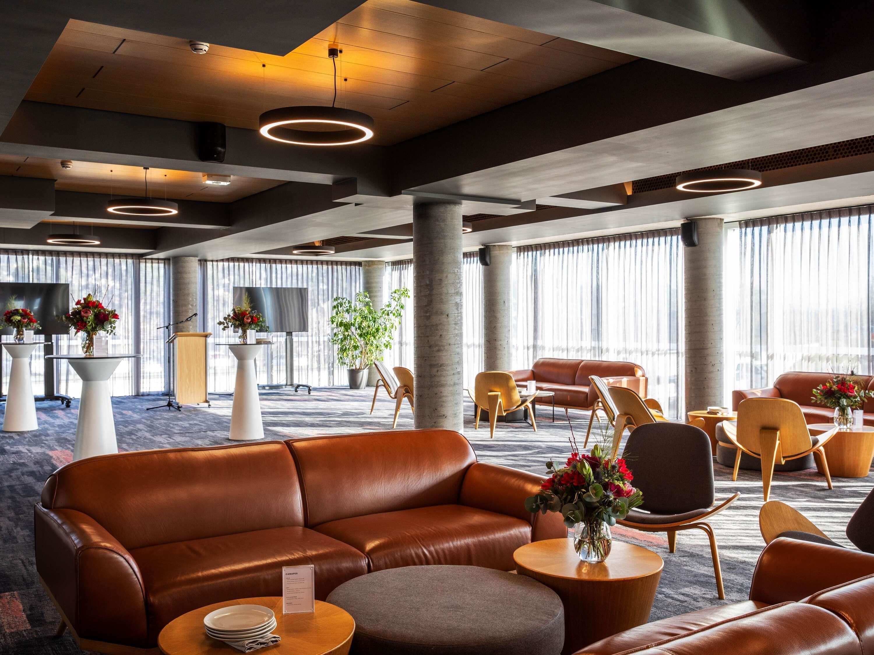 A modern hotel lobby with leather sofas, round tables, and large windows.