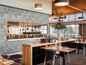 A restaurant with a bar area, wooden tables, black chairs, and hanging pendant lights. - Peppers Silo Launceston (Invermay)
